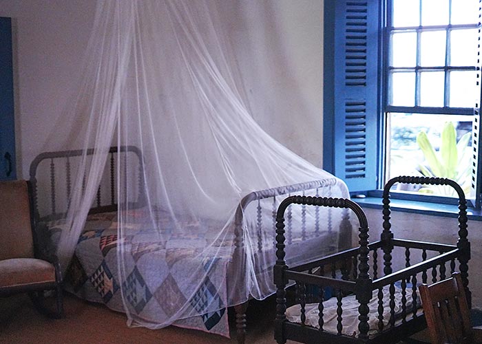 image of a bed with mosquito netting and a baby's crib. 